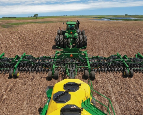 Photo shows a large tractor with an attached planting implement and tanks with seed and fertilizer.