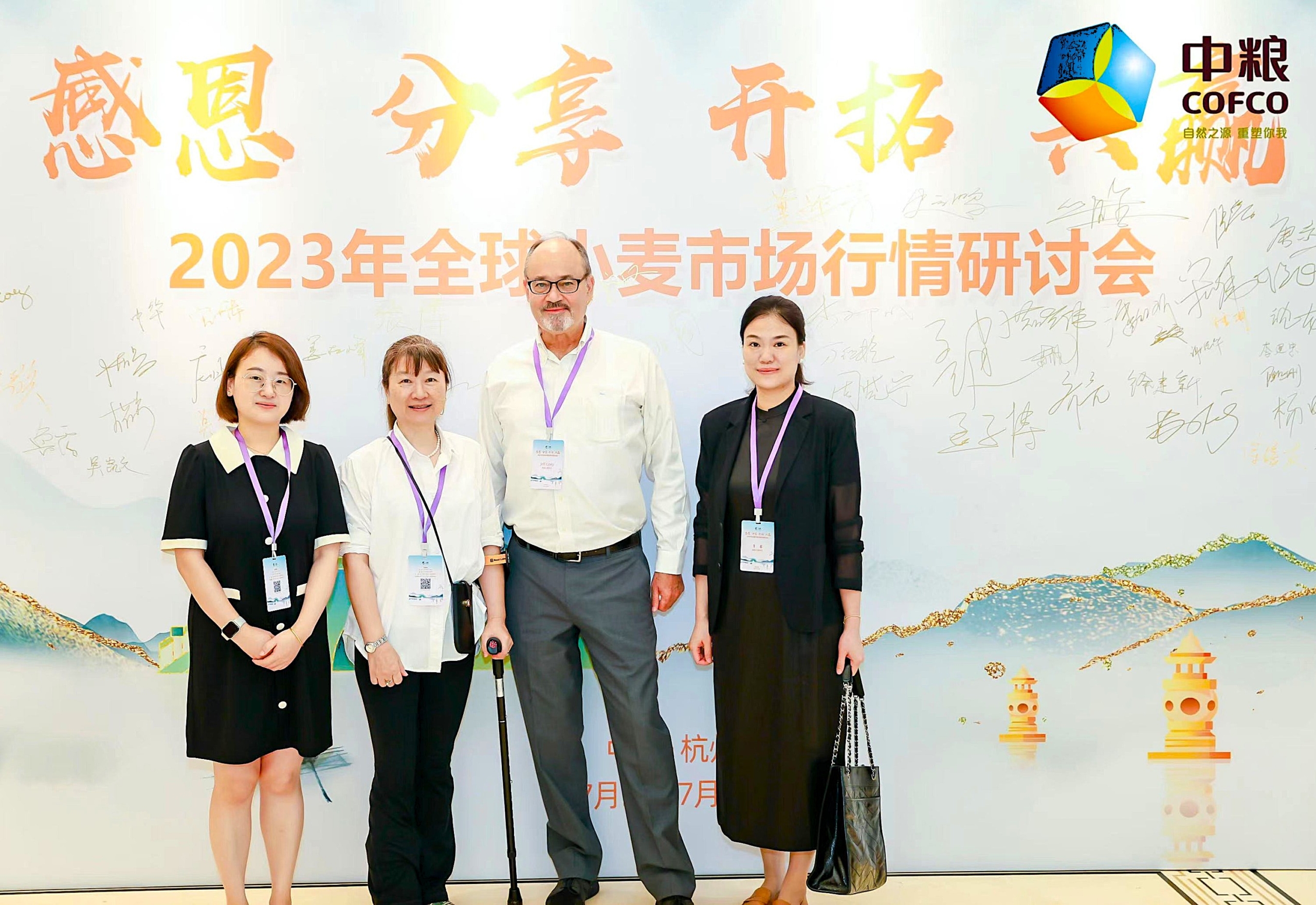 Photo of 4 people standing in front of a backdrop with Chinese characters and landscape drawing.